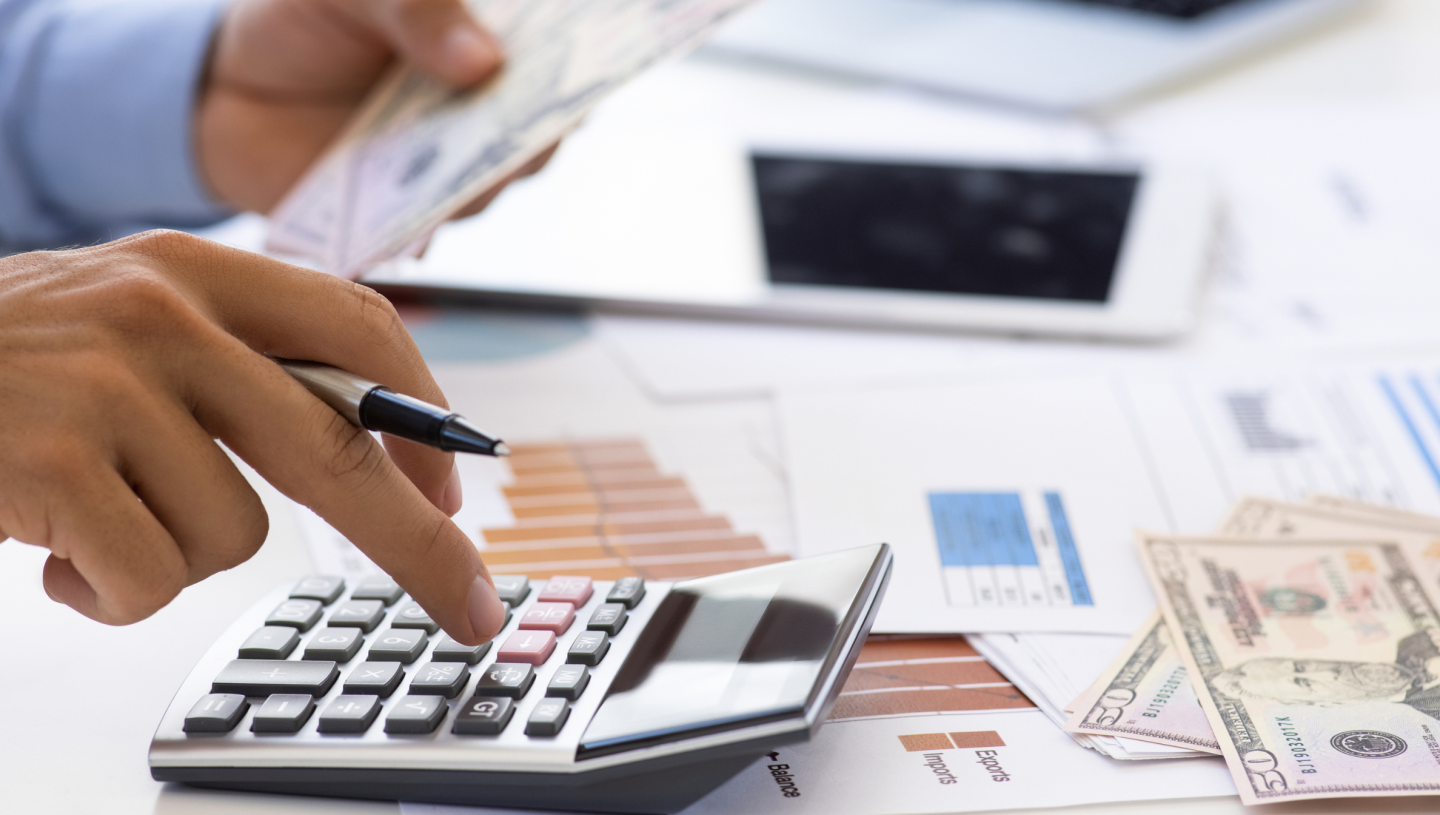 Image of Hands typing on a calculator, with money and financial documents on the table.