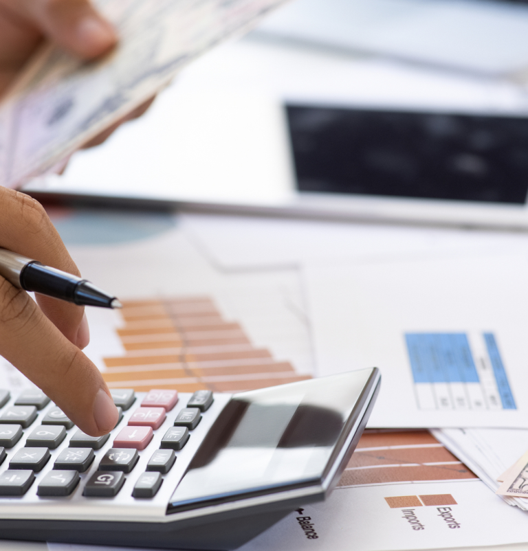 Image of Hands typing on a calculator, with money and financial documents on the table.