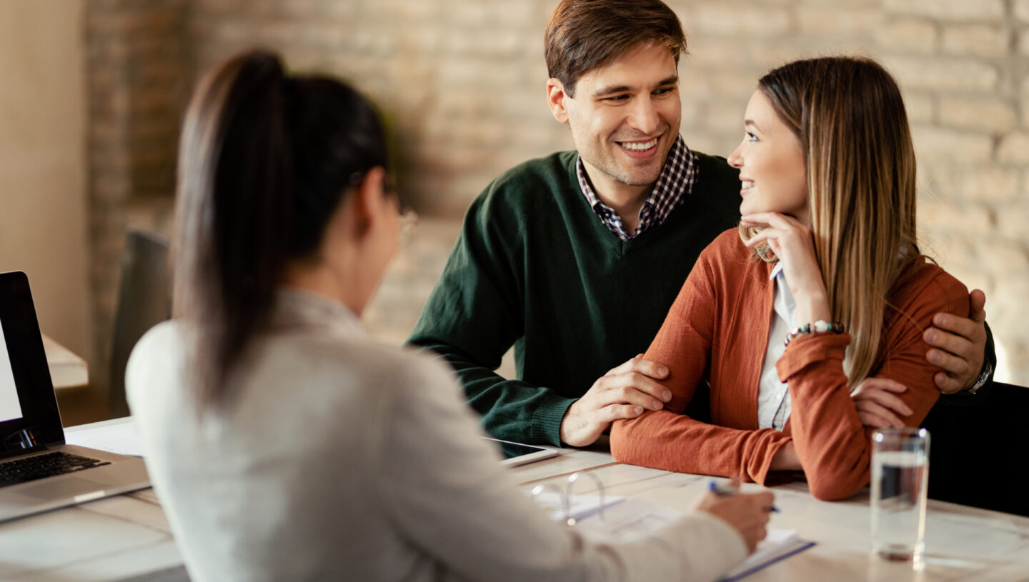 Young smiling couple communicating while being on a meeting with financial advisor.