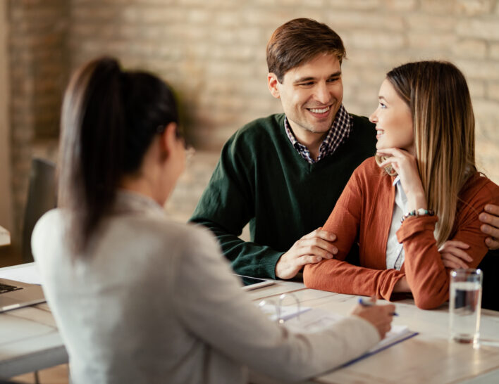 Young smiling couple communicating while being on a meeting with financial advisor.