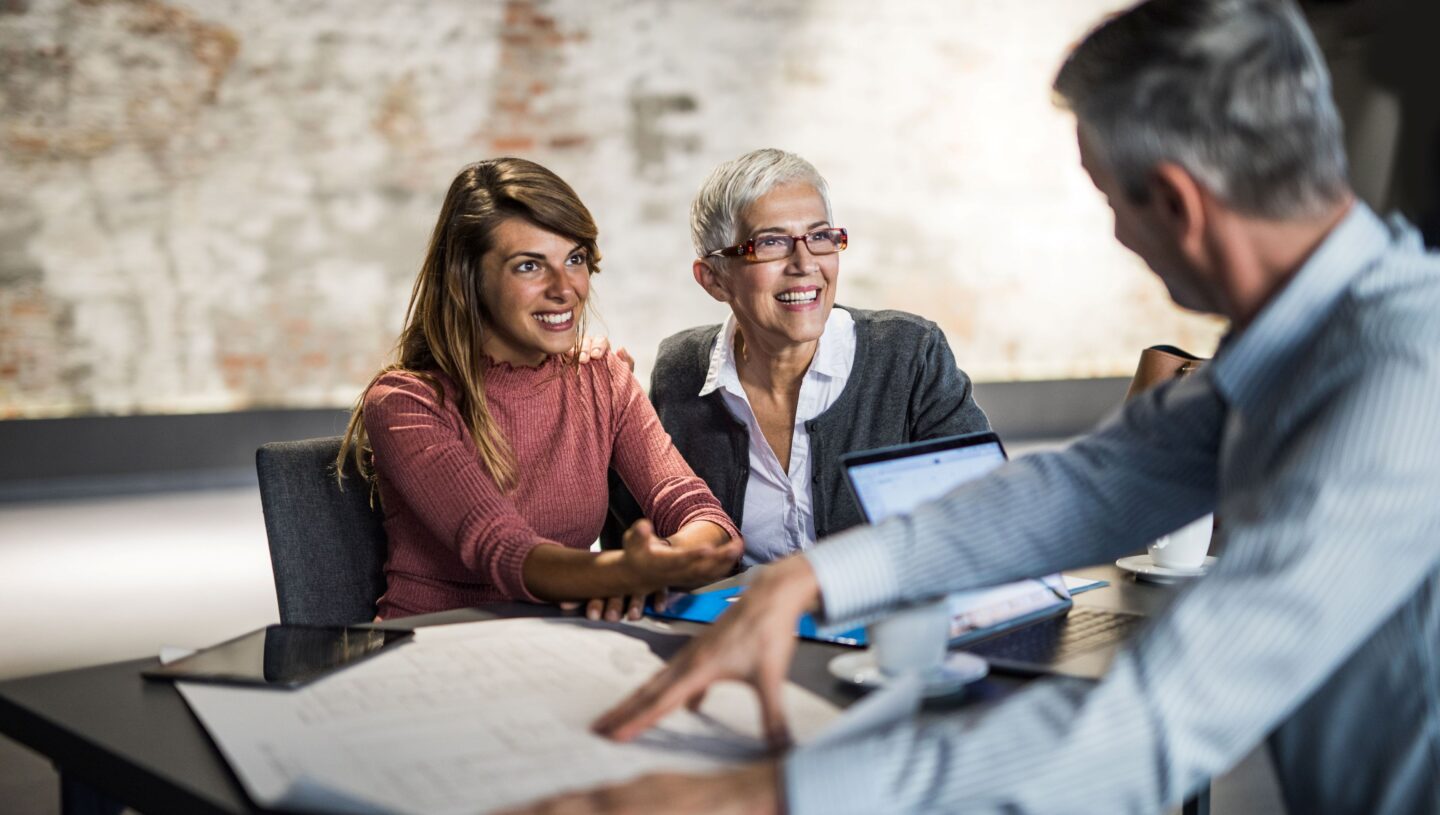 Women smiling during a business meeting with a man discussing documents at a table in a modern office.
