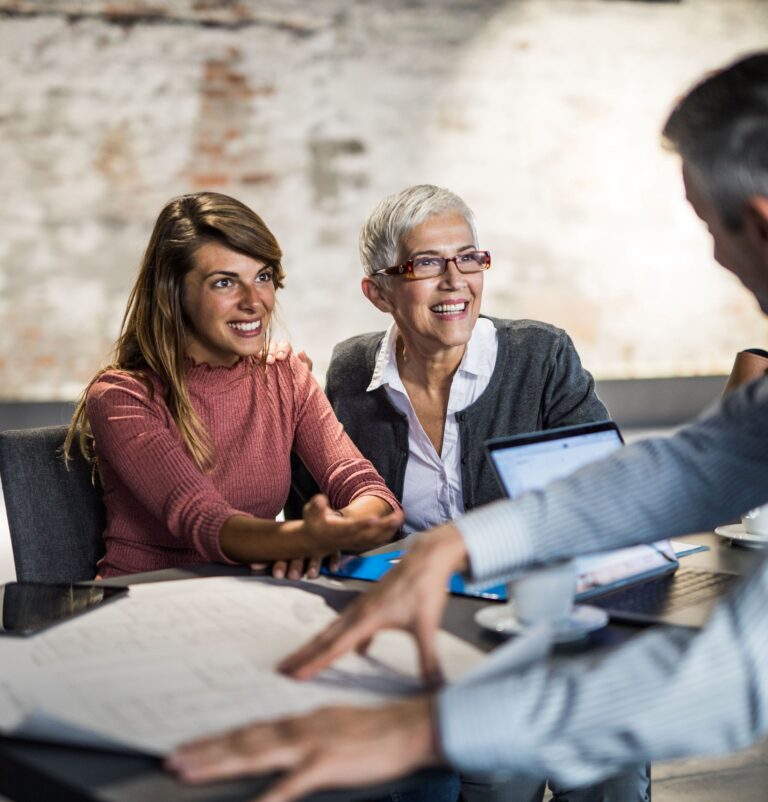 Women smiling during a business meeting with a man discussing documents at a table in a modern office.