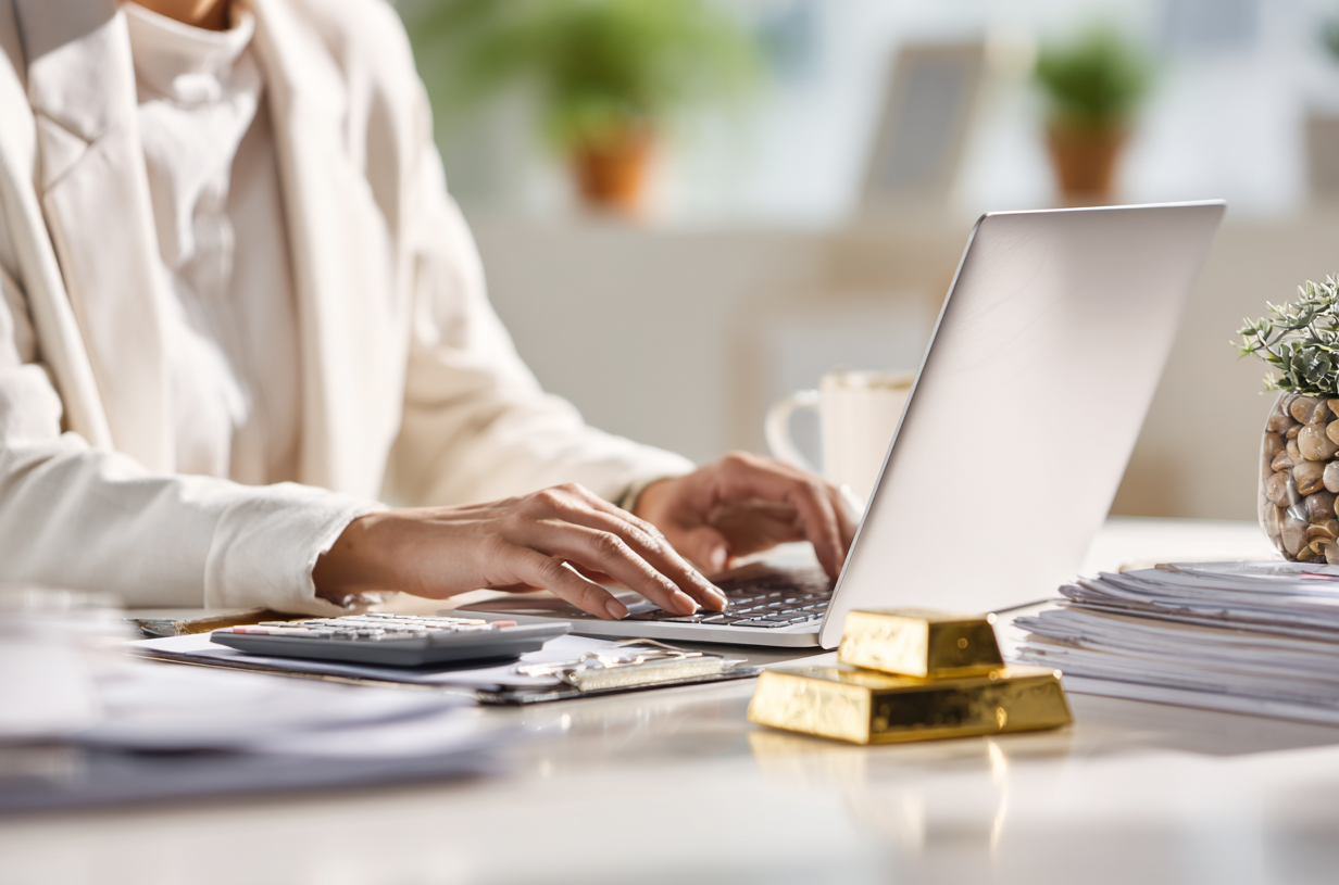 An SMSF professional working on a laptop, while gold bouillon sits on her desk.